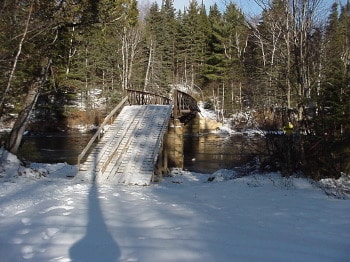 A snow covered river flowing beneath a wooden bridge in the Forks area.